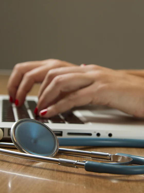 Clinician working on a laptop beside a stethoscope